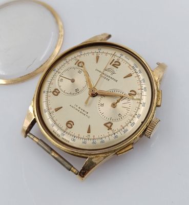 une montre en or et une loupe posées sur une surface blanche