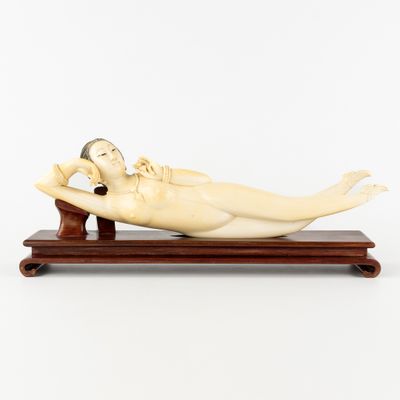 une figurine en ivoire représentant une femme allongée, posée sur un socle en bois
