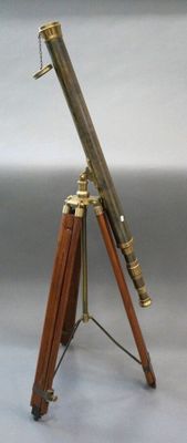 an antique brass telescope on a wooden tripod stand on a gray background