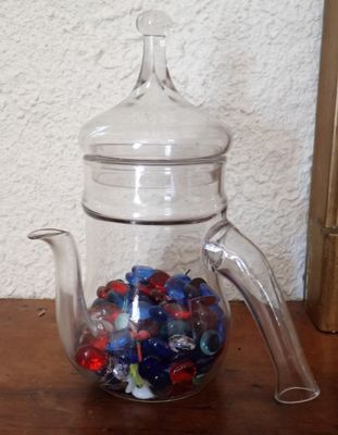 une théière en verre remplie de billes, posée sur une table