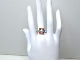 une main blanche sur laquelle se trouve une bague ornée d'un anneau multicolore