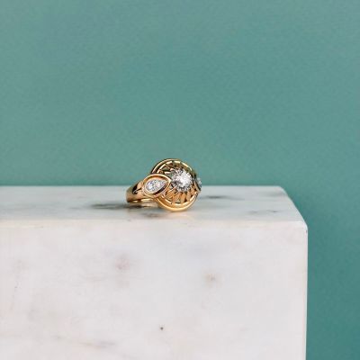 un gros plan d'une bague en or sertie d'un diamant, posée sur un bloc de marbre