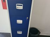 a blue filing cabinet with three drawers next to a trash can