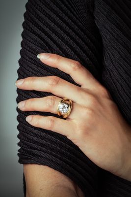 woman ' s hand wearing a gold ring with a diamond on it