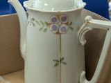a white tea pot with purple flowers on it in a box