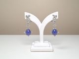 des boucles d'oreilles ornées de perles de verre bleues, posées sur un support blanc sur une table