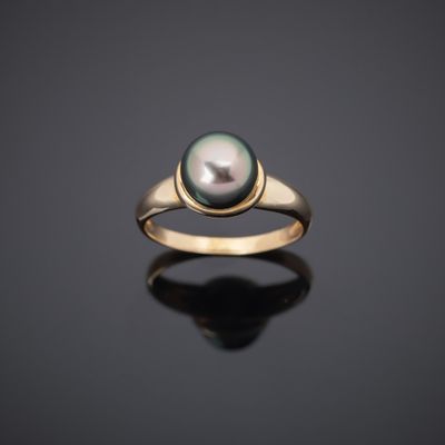 a black pearl and gold ring on a black surface