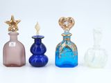 Quatre bouteilles en verre de couleurs différentes sont alignées sur une surface blanche.