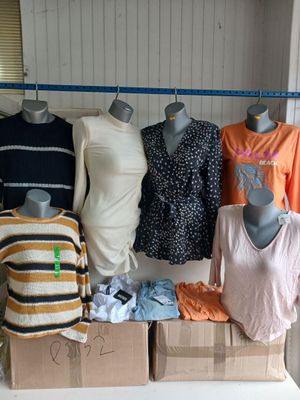 Plusieurs mannequins sont alignés sur une table, à côté de cartons de vêtements