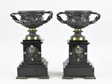 paire de vases noirs et dorés ornés de têtes de lion, posés sur des socles