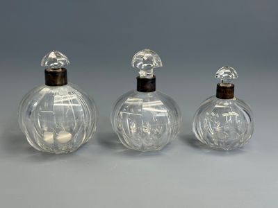 three clear glass perfume bottles with wooden lids on a gray surface