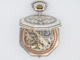 une montre de poche en argent et en or posée sur une surface blanche