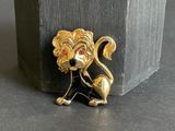 a gold lion brooch with a red stone in the background