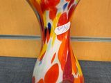 a colorful vase sitting on the floor in front of a wooden wall
