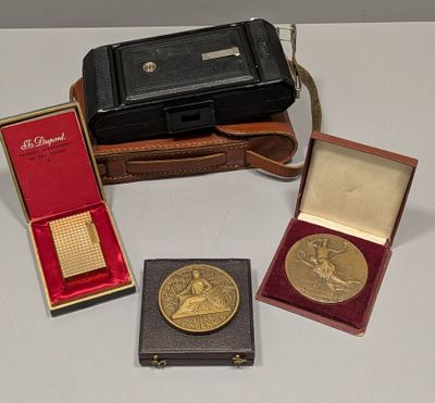 trois médailles d'or et un étui en cuir posés sur une surface blanche