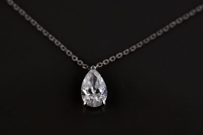 a pear shaped diamond pendant hangs from a chain on a black surface