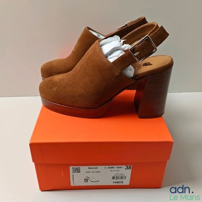 une paire de mules en daim marron à talon en bois, posée sur une boîte orange