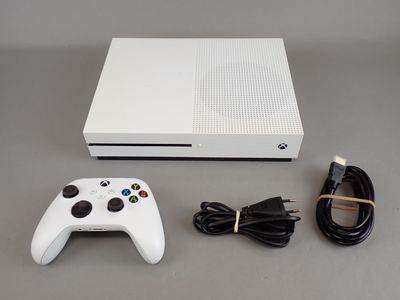 the white xbox one is sitting next to a charger and a cable