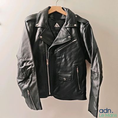 une veste en cuir noir suspendue à un cintre sur un mur blanc