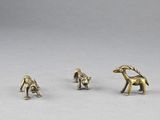 three brass figurines of dogs and a cat on a white surface