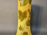 un vase jaune orné de feuilles, posé sur une table