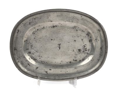 un vieux plat en argent posé sur un socle, sur une surface blanche
