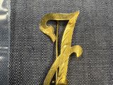 un gros plan sur une broche en or sur laquelle figure la lettre « f »