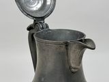 an old metal pitcher with a lid on a white surface