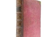 an old book with a pink cover sitting on top of a white surface