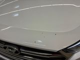 the front of a white car with a dent on it ' s hood