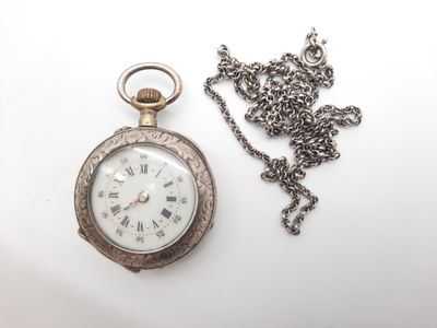 une montre de poche en argent et une chaîne posées sur une surface blanche
