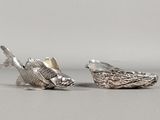 une paire de figurines de poissons en argent posées sur un support gris