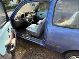 une petite voiture bleue dont la portière est ouverte et dans laquelle se trouve un chien sur le siège passager