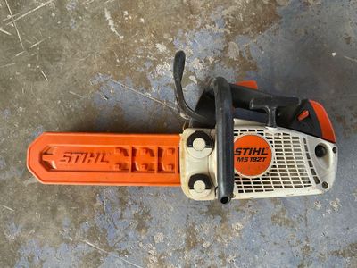 une tronçonneuse orange et noire posée sur un sol en béton