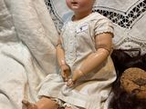 a doll that is sitting on a bed with a teddy bear