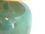a green vase sitting on a table with a lamp on it