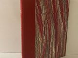 un livre rouge à la couverture rayée posé sur une table blanche