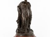 une statue en bronze représentant une femme tenant un enfant dans ses bras, posée sur un socle en marbre