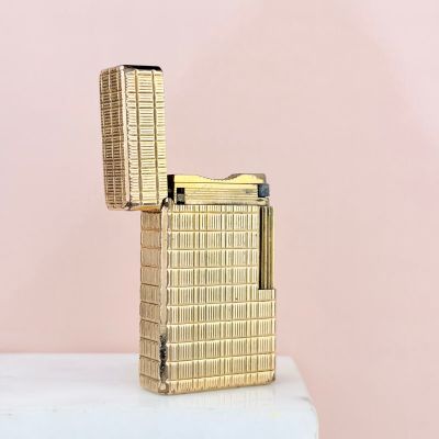 un briquet doré posé sur une table blanche près d'un mur rose