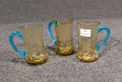 trois tasses en verre jaune avec des anses bleues posées sur une surface grise