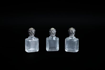 trois bouteilles en verre transparent munies de bouchons argentés sont posées sur une surface noire