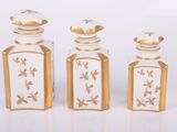 trois bouteilles en verre ornées de motifs dorés, disposées les unes à côté des autres
