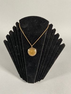 a gold necklace with a coin on a black display stand