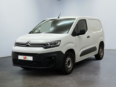 La camionnette blanche est garée dans une grande pièce où se trouve une horloge accrochée au mur.