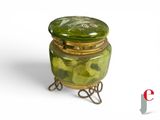 a green glass jar with a gold lid on a stand