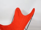 an orange butterfly chair with a black metal frame on a white background