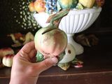 a person holding a small figurine in front of a bowl of fruit