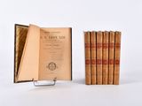 Plusieurs livres anciens sont empilés sur un présentoir devant un fond blanc.