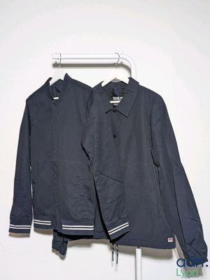 two jackets hanging on a hanger in front of a white wall