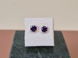 une paire de boucles d'oreilles en saphir violet posées sur un bloc de marbre